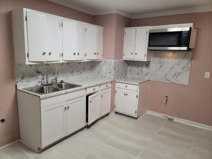 A kitchen with white cabinets and pink walls.