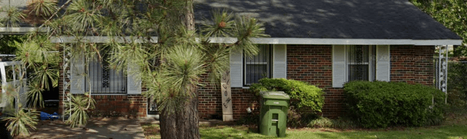 Brick house with green bushes and a trash can.