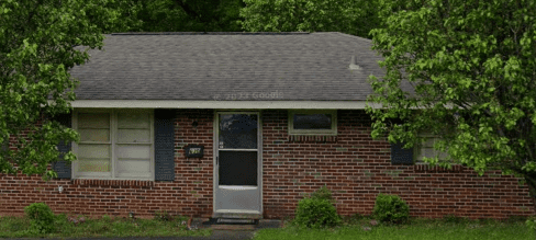 Brick ranch house with green trees.