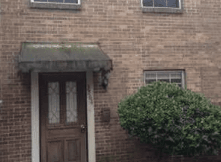 Brick townhouse with brown door and shrubs.