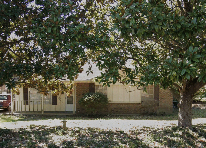 House behind large trees and front yard.